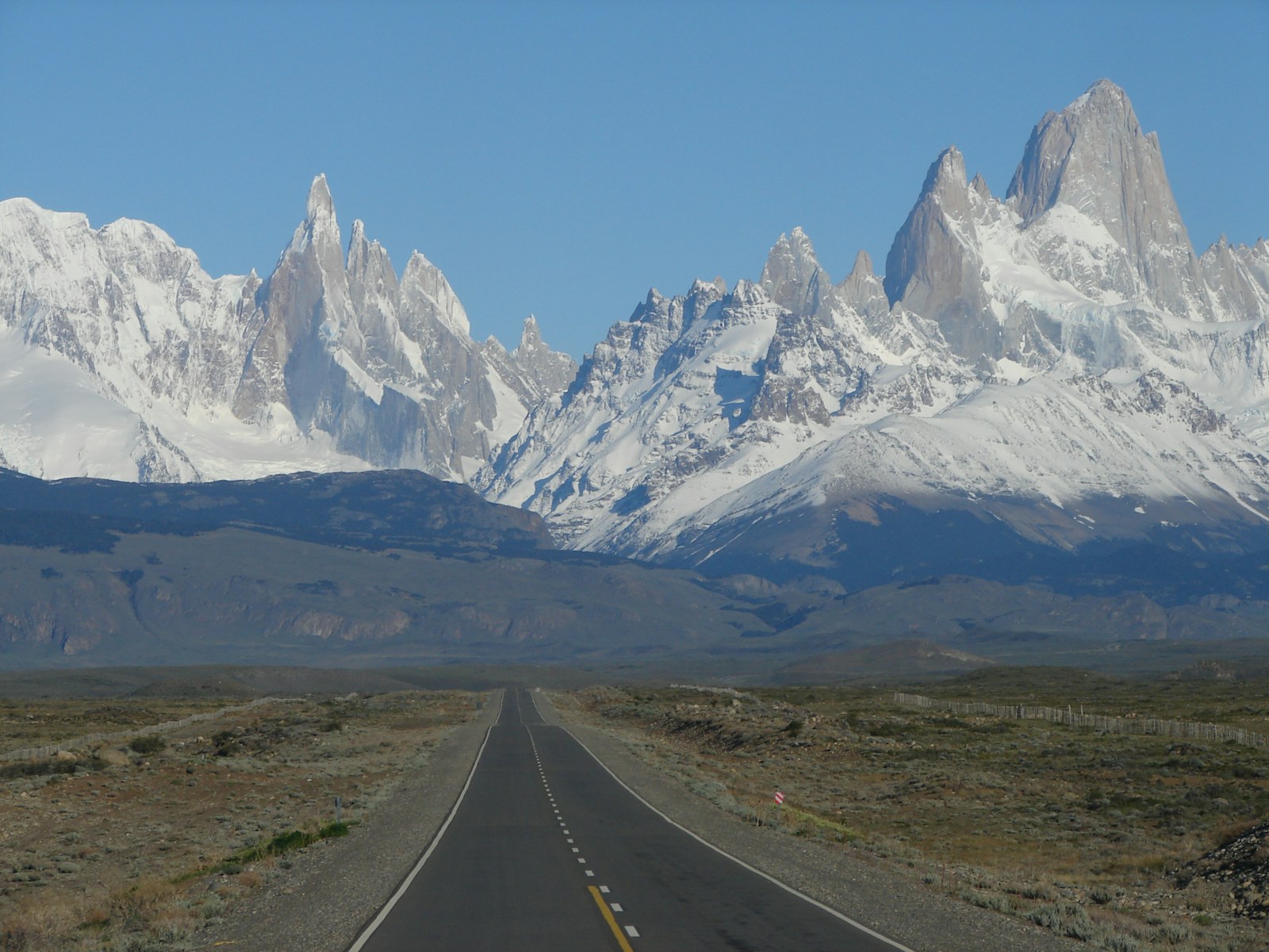 Estrada cruzando a estepe patagônica com montanhas nevadas ao fundo